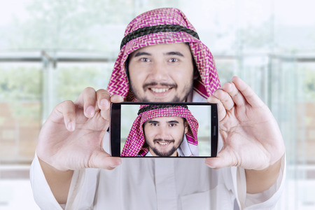 Portrait of Arabian businessman taking selfie photo with a smartphone in the office lobbyの写真素材