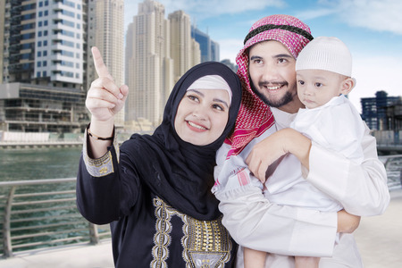 Happy middle eastern family wearing islamic clothes and looking at something in the cityの写真素材