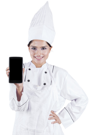 Picture of a female chef showing a smartphone while smiling at the camera in the studioの写真素材