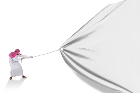 Young Arabic person wearing traditional clothes and pulling a big banner in the studioの写真素材