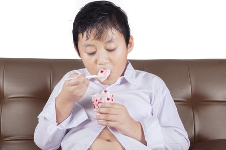 Portrait of a little boy with potbelly sitting on the sofa while eating ice cream on the sofaの写真素材