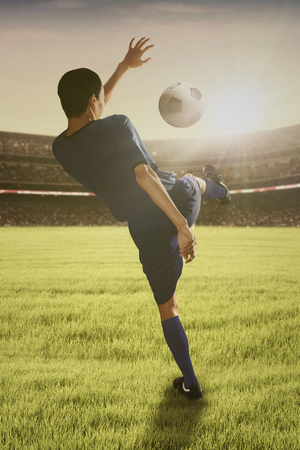 Portrait of young football player kicking a ball on the soccer fieldの写真素材