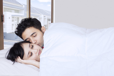 Portrait of young couple sleeping on bed and covered by a blanket with residential background on the windowの写真素材