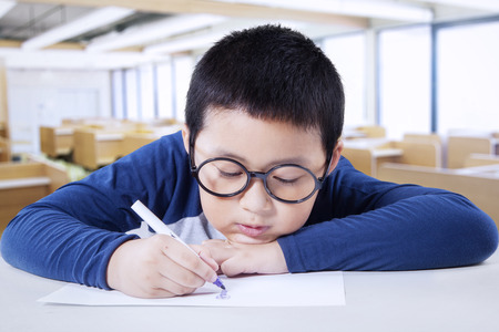 Portrait of a little schoolboy drawing a picture on the paper at desk, shot in the classroomの写真素材
