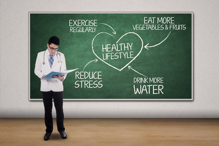 Portrait of a male doctor reads a document with plan for healthy lifestyle on the blackboardの写真素材