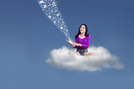 Female high school student sending message with a digital tablet while sitting on the cloudの写真素材