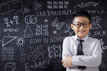 Handsome little boy standing in the class while smiling at the camera with doodle on the blackboardの写真素材