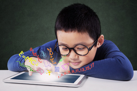 Photo of a little boy using a digital tablet to learn with formula of math on the screen