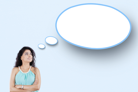 Young Indian woman thinking idea while looking at a blank speech bubbleの写真素材