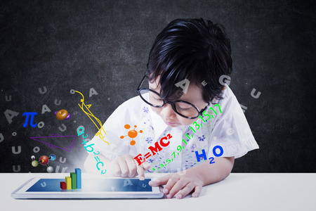 Female elementary school student using a digital tablet for studying with formula of science, math,...