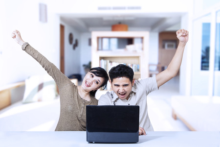 Happy couple winning at home, working with laptopの写真素材