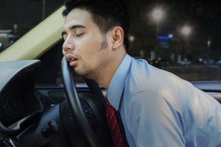 Young businessman looks tired and sleeping inside a car on the steering wheel