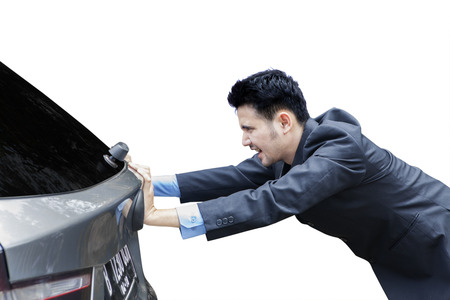 Frustrated businessman pushing a broken car while wearing business suit, isolated on white backgroundの写真素材