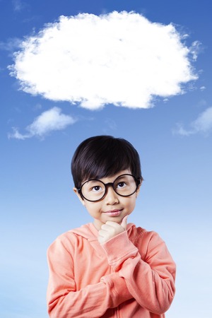 Portrait of a cute little girl wearing glasses and thinking under white cloudの写真素材