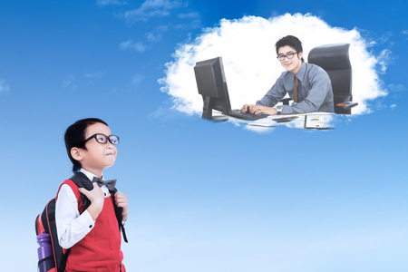 Cute elementary school student wearing uniform while looking at a businessman working on the cloudの写真素材