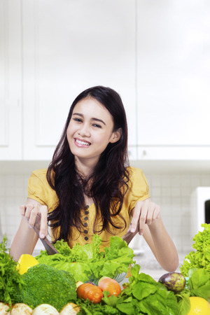 Young woman smiling at the camera while making salad with organic vegetable in the kitchenの写真素材