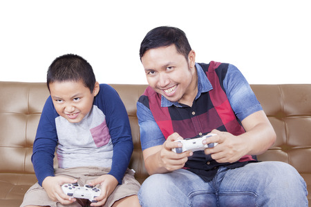 Portrait of cheerful father and his son playing video games while sitting on the sofa, isolated on...