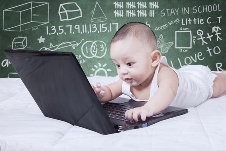 Adorable baby boy playing laptop computer on the laptop with doodles on the chalkboardの写真素材