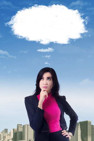 Portrait of a pensive businesswoman looking at cloud on the sky with hands on her chinの写真素材