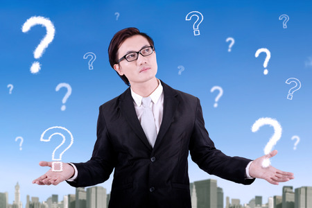 Picture of a pensive young businessman wearing formal suit with question mark on the skyの写真素材