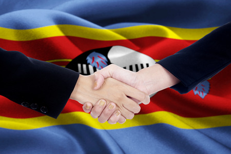 Photo of a friendship handshake with two people hands, shaking hands in front of a national flag of Swazilandの写真素材
