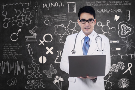 Male doctor holding a laptop on blackboard backgroundの写真素材