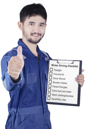 Portrait of a male workshop worker showing thumb up while holding a clipboard with winter driving tipsの写真素材