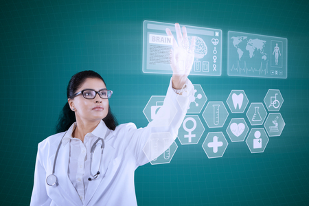 Image of Indian doctor standing and pressing icon brain on virtual screen with stethoscope and glassesの写真素材