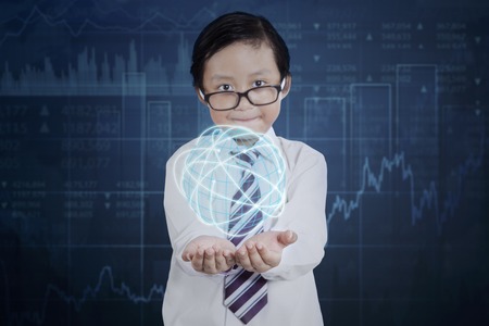 Little boy wearing glasses and holding a globe with internet connection symbol and financial statistic backgroundの写真素材