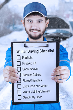 Young Asian mechanic holding a clipboard and showing a winter driving tips, shot outdoorsの写真素材