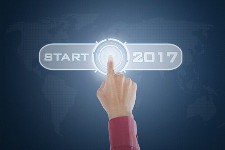 Close up of businessperson hand touching a virtual start button with number 2017 on the futuristic interfaceの写真素材