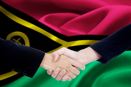 Two hands of business people shaking hands with flag of Vanuatu blowing in the windの写真素材