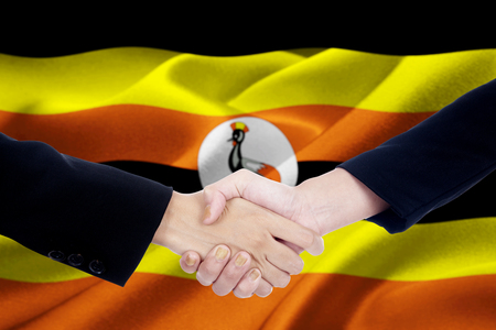 Photo of two entrepreneurs shaking hands with flag of Uganda blowing in the windの写真素材