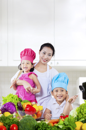 Portrait of happy mother with her two children preparing a salad in the kitchen at homeの写真素材