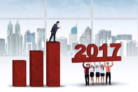 Group of worker trying to build a financial graph with number 2017, symbolizing good team work for the futureの写真素材