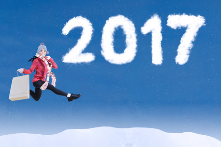 Young woman leaping on the sky with clouds shaped number 2017 while carrying shopping bag