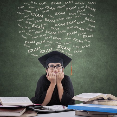 Portrait of female student with gown, biting her nails and looks nervous to face exam