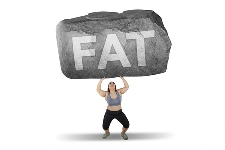 Obese woman lifting a big stone with fat word while standing in studio, isolated on white backgroundの写真素材