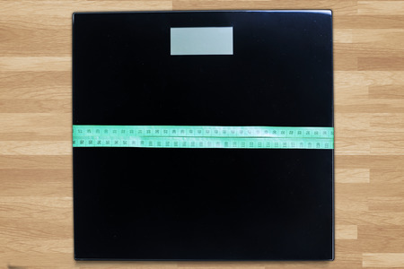 Image of scales with a green measuring tape on the wooden floor
