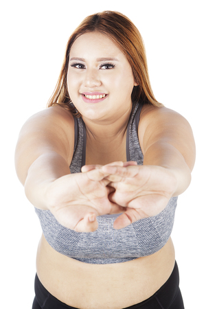 Image of obese female smiling at the camera while doing warm up by stretching her hands on the studioの写真素材
