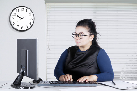 Portrait of young woman typing on keyboard while sitting in front of her computer in the officeの写真素材