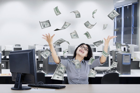 Beautiful businesswoman looking dollars money flying over her head while raising handsの写真素材
