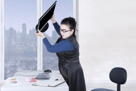 Female entrepreneur throws computer with financial chart on the desk, winter background on the windowの写真素材
