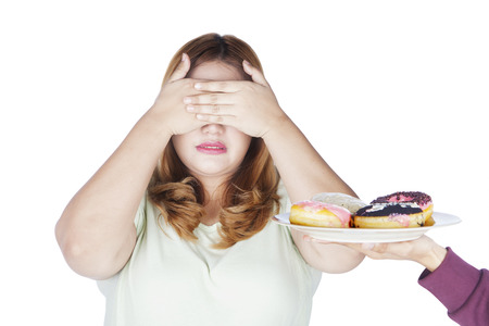Portrait of overweight woman closed her eyes for a plate of donuts, isolated on white backgroundの写真素材