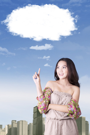Portrait of young woman getting idea while standing under bubble cloudの写真素材
