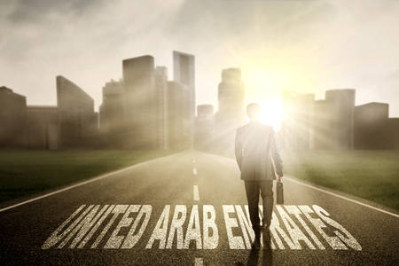 Businessman walking on the street while carrying a briefcase with United Arab Emirates word at sunriseの写真素材