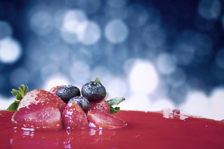 Picture of fruity cake decorated with strawberry and blueberry against light bokeh background