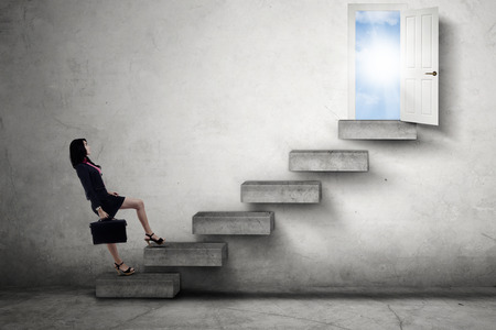Young businesswoman walking on the stairs leads to an opportunity doorの写真素材