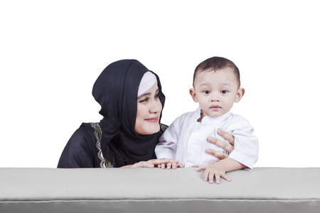 Portrait of arabian mother smiling at her cute child while sitting on the sofa, isolated on white backgroundの写真素材