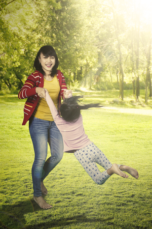 Happy young woman and her little daughter playing together at the park while holding handsの写真素材